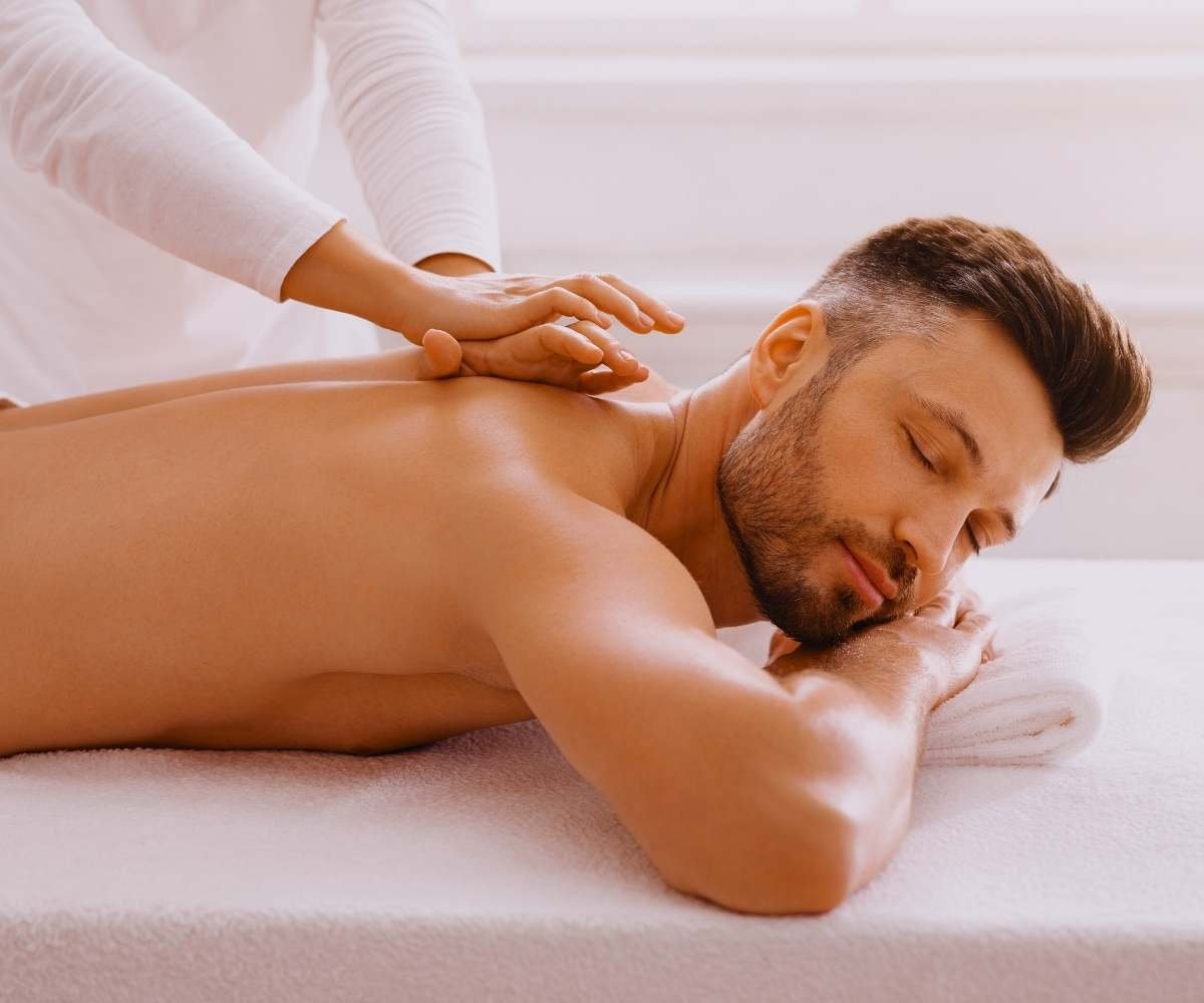 A man receiving a therapeutic deep tissue back massage from a therapist, illustrating muscle pain relief and relaxation at Queen Palace Hotel Spa.